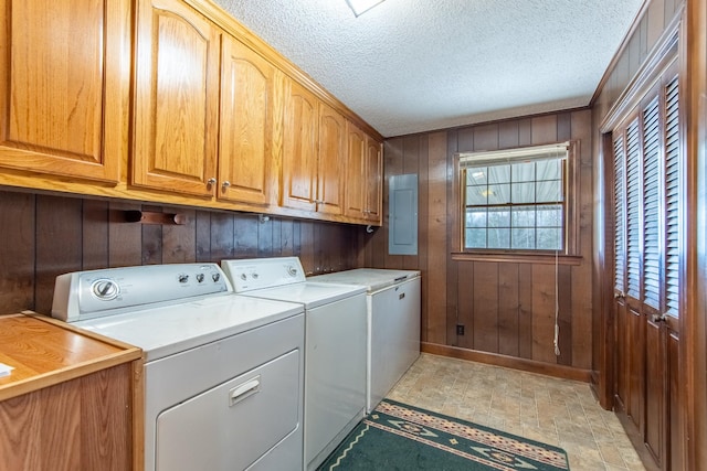 washroom with washer and dryer, wooden walls, cabinets, electric panel, and a textured ceiling