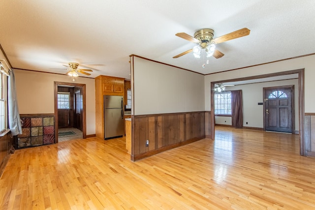 unfurnished living room featuring ornamental molding, ceiling fan, and light hardwood / wood-style flooring