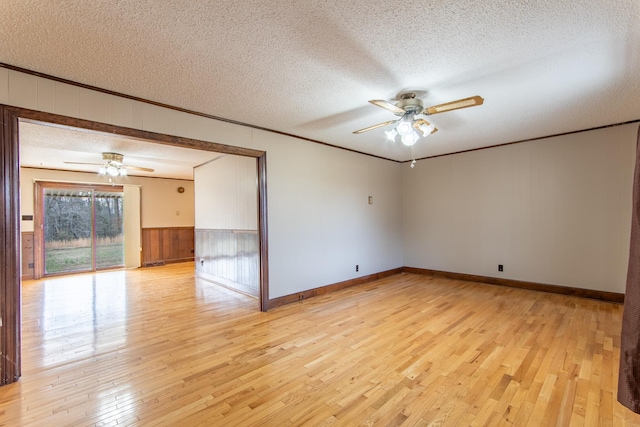 unfurnished room featuring wooden walls, ornamental molding, ceiling fan, light hardwood / wood-style floors, and a textured ceiling