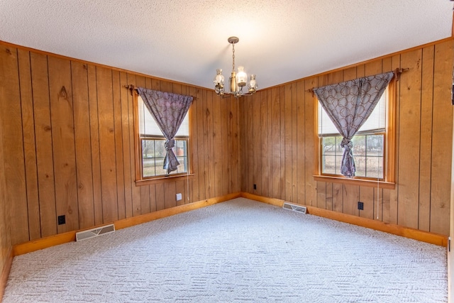 carpeted spare room featuring wooden walls, a textured ceiling, and an inviting chandelier