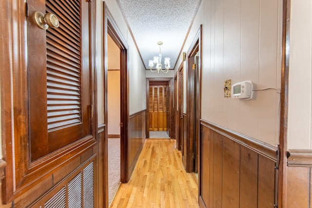 hall featuring light wood-type flooring, a notable chandelier, a textured ceiling, and wood walls