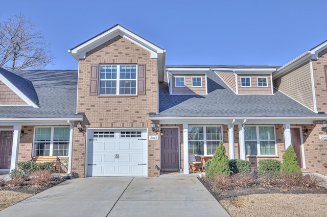 view of front facade with roof with shingles, concrete driveway, and brick siding