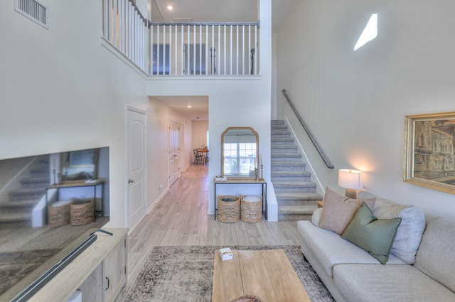 living area featuring light wood finished floors, stairway, a towering ceiling, and visible vents