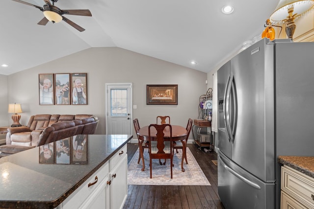 kitchen featuring dark wood-type flooring, lofted ceiling, stainless steel fridge, dark stone counters, and white cabinets