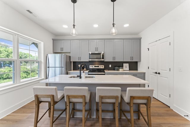 kitchen featuring appliances with stainless steel finishes, sink, a center island with sink, and gray cabinetry