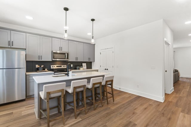 kitchen featuring gray cabinets, appliances with stainless steel finishes, sink, backsplash, and a center island with sink