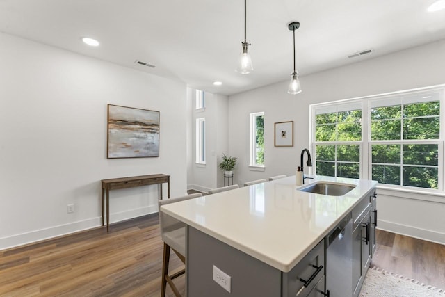 kitchen featuring dark wood-type flooring, sink, stainless steel dishwasher, pendant lighting, and a kitchen island with sink