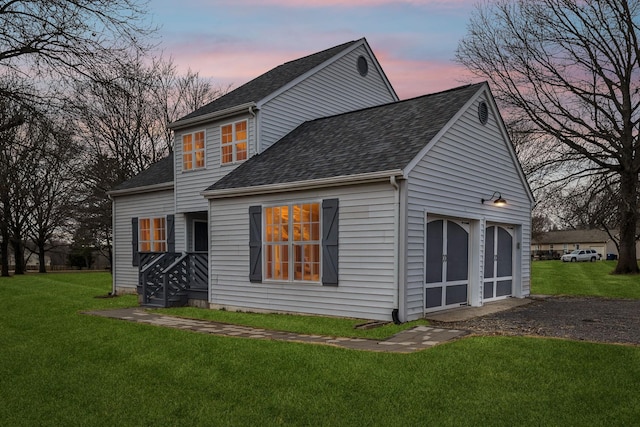 back house at dusk with a garage and a lawn