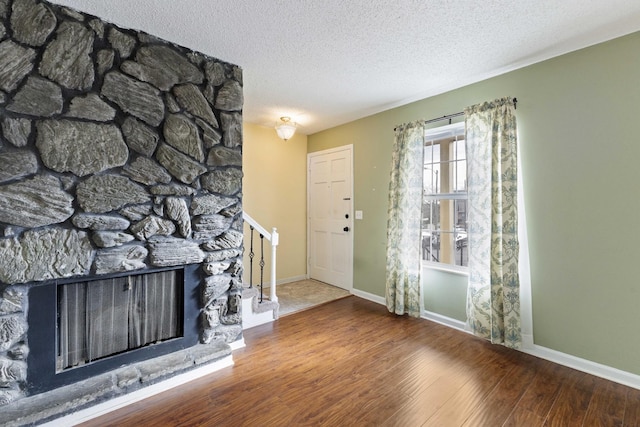 entryway with wood-type flooring, a stone fireplace, and a textured ceiling