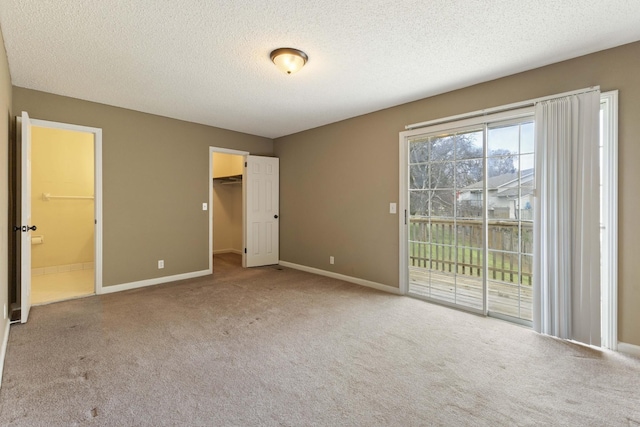 unfurnished bedroom featuring ensuite bathroom, carpet, a spacious closet, access to outside, and a textured ceiling