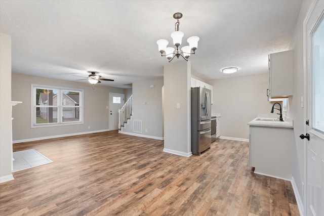 unfurnished living room with ceiling fan with notable chandelier, sink, hardwood / wood-style floors, and a textured ceiling