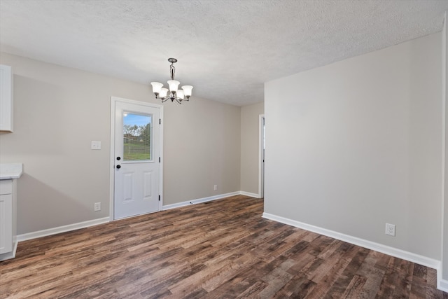 unfurnished dining area with dark wood-type flooring, an inviting chandelier, and a textured ceiling