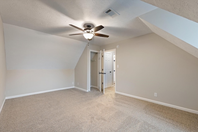 additional living space with vaulted ceiling, light colored carpet, ceiling fan, and a textured ceiling