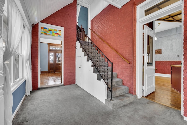 carpeted entryway featuring high vaulted ceiling and brick wall