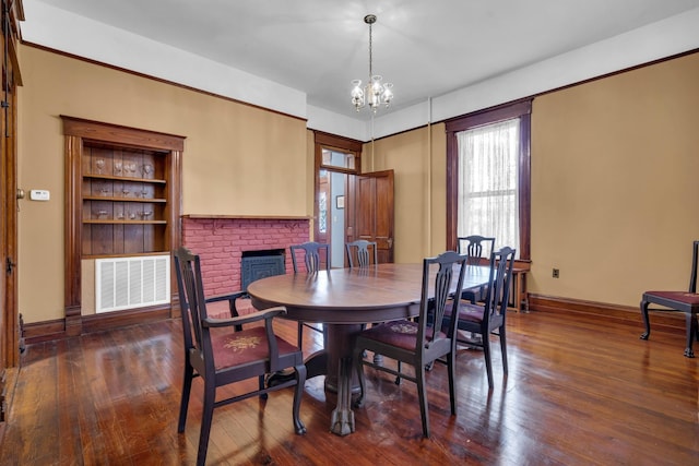 dining room featuring a brick fireplace, dark hardwood / wood-style floors, and an inviting chandelier