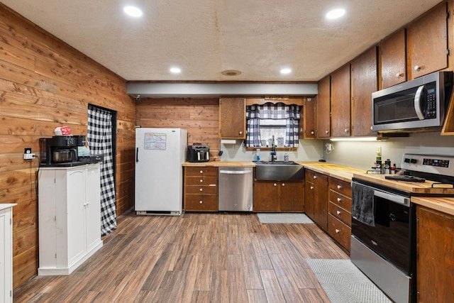 kitchen with appliances with stainless steel finishes, dark hardwood / wood-style floors, wooden walls, sink, and a textured ceiling