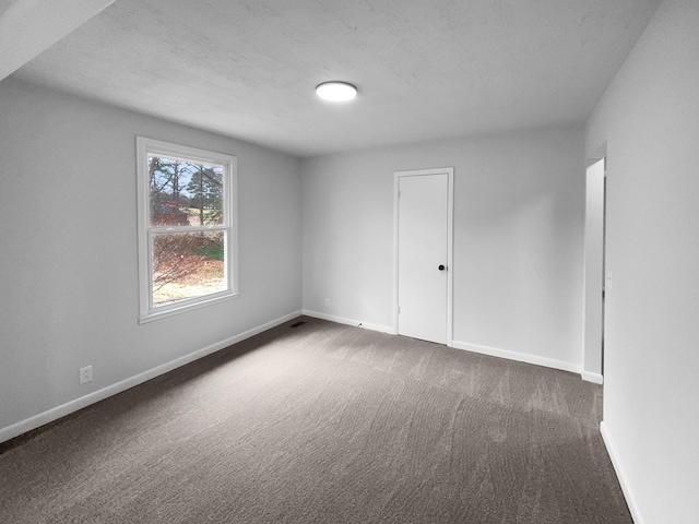 spare room with a textured ceiling and dark colored carpet