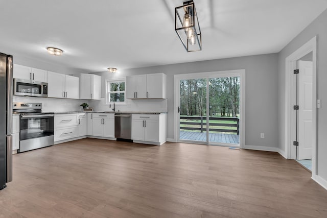 kitchen with decorative backsplash, appliances with stainless steel finishes, light hardwood / wood-style flooring, and white cabinets