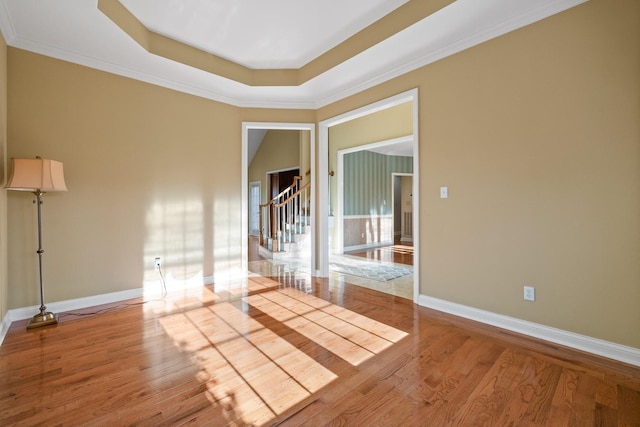 spare room featuring crown molding, light wood-type flooring, and a tray ceiling