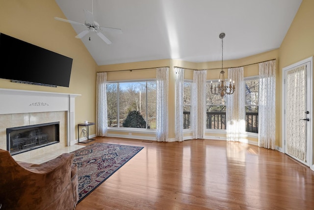 living room featuring a tile fireplace, ceiling fan with notable chandelier, a wealth of natural light, and light hardwood / wood-style floors