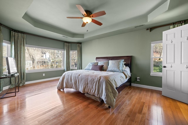 bedroom with ceiling fan, wood-type flooring, and a tray ceiling