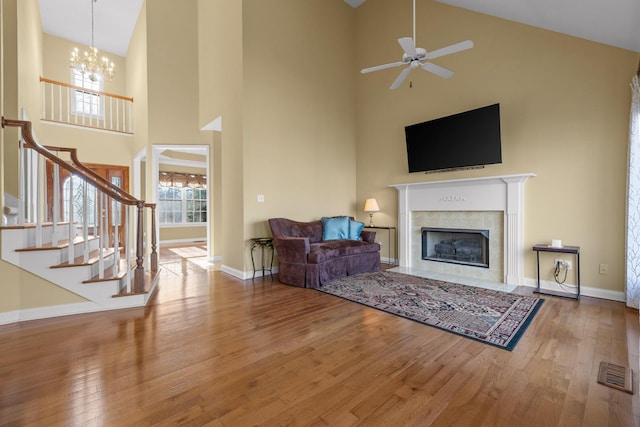 living room featuring hardwood / wood-style flooring, a towering ceiling, ceiling fan with notable chandelier, and a fireplace