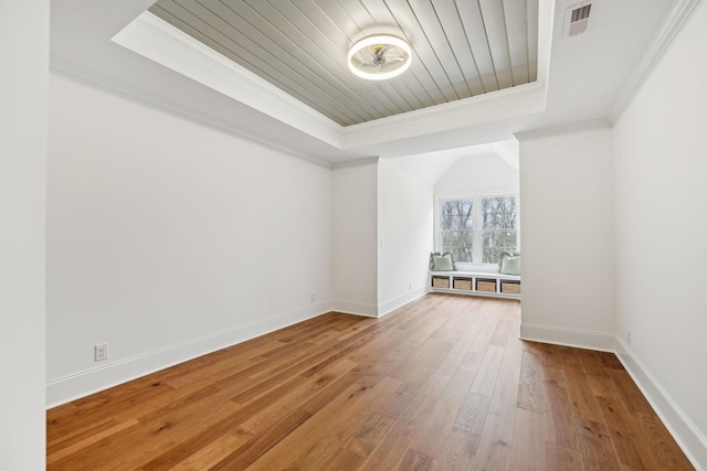 empty room with crown molding, baseboards, a raised ceiling, and wood finished floors