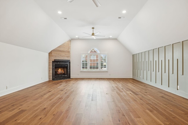 unfurnished living room featuring ceiling fan, lofted ceiling, a stone fireplace, light wood-style flooring, and visible vents