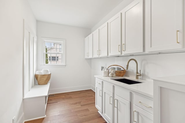 washroom with cabinet space, baseboards, hookup for a washing machine, light wood-type flooring, and a sink