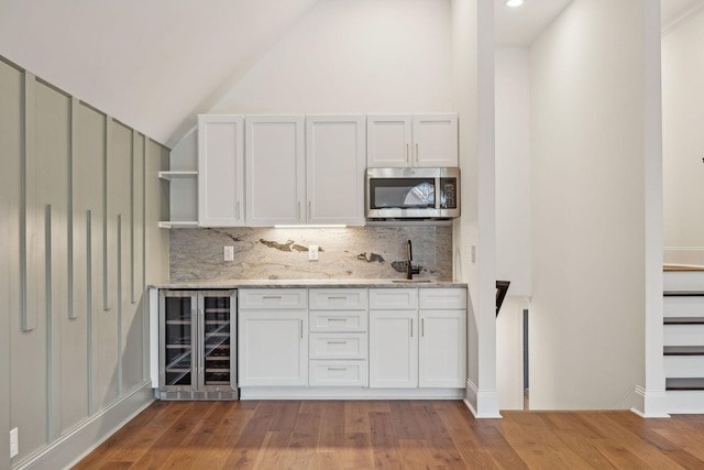 bar featuring light wood-style floors, wine cooler, stainless steel microwave, and decorative backsplash