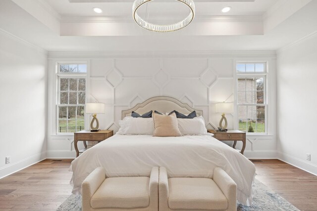 bedroom with baseboards, light wood-style flooring, a tray ceiling, and crown molding