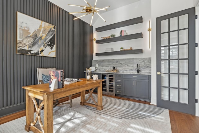 office space featuring beverage cooler, wet bar, light wood-style floors, a chandelier, and a sink