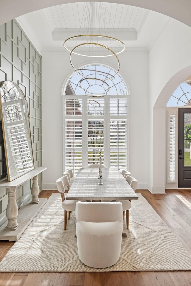 dining area with a chandelier, arched walkways, crown molding, and light wood-style flooring