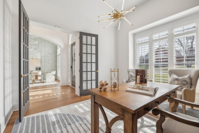 home office featuring arched walkways, french doors, wood finished floors, and a notable chandelier