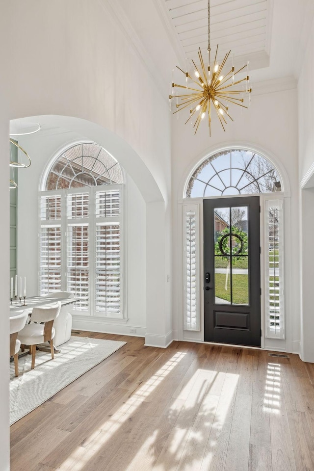 foyer entrance featuring a chandelier, crown molding, a towering ceiling, and wood finished floors