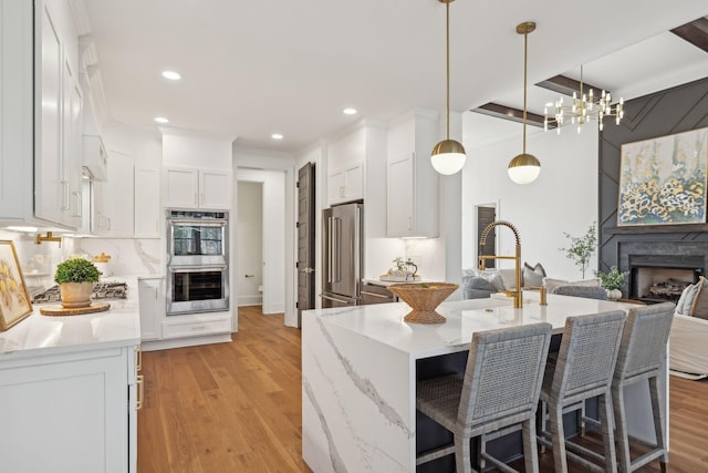 kitchen featuring light stone counters, a breakfast bar area, hanging light fixtures, appliances with stainless steel finishes, and white cabinetry