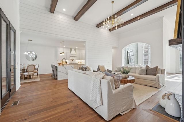 living area featuring wood finished floors, visible vents, baseboards, beam ceiling, and an inviting chandelier