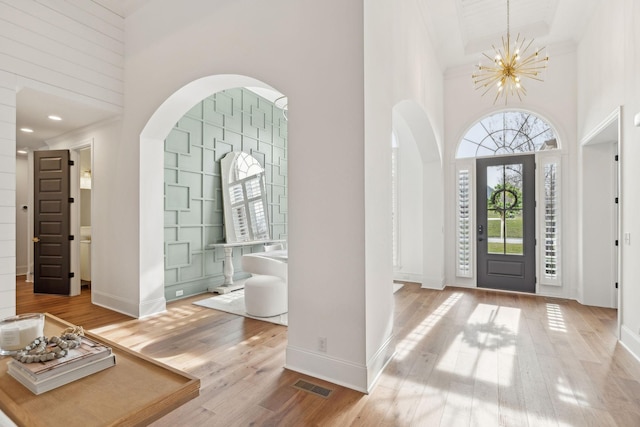 foyer entrance with arched walkways, visible vents, a high ceiling, an inviting chandelier, and light wood-type flooring