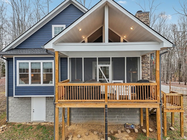 back of house featuring a sunroom, roof with shingles, a chimney, and a wooden deck