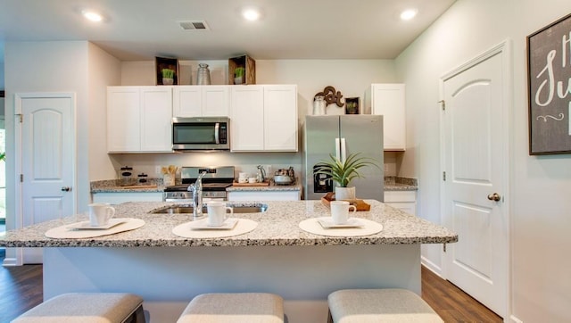 kitchen featuring dark wood-type flooring, a center island with sink, appliances with stainless steel finishes, light stone countertops, and white cabinets