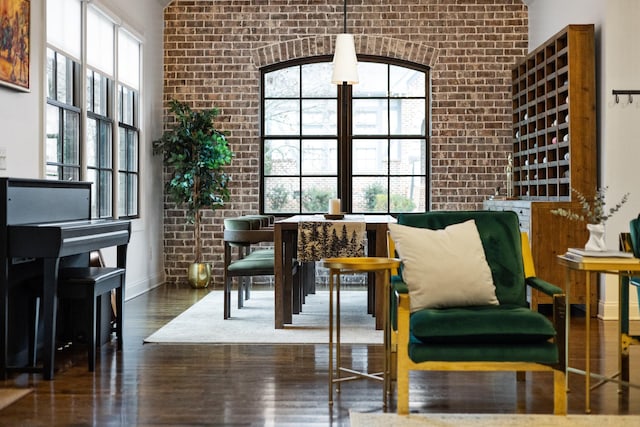 living area with baseboards, a healthy amount of sunlight, brick wall, and wood finished floors