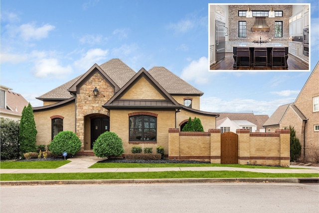 view of front of home with stone siding, a fenced front yard, roof with shingles, a gate, and brick siding