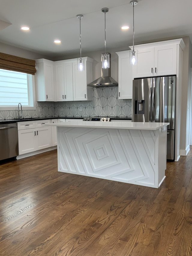 kitchen with pendant lighting, wall chimney range hood, appliances with stainless steel finishes, white cabinets, and a kitchen island