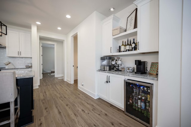 bar with white cabinets, wine cooler, backsplash, light stone countertops, and light hardwood / wood-style flooring