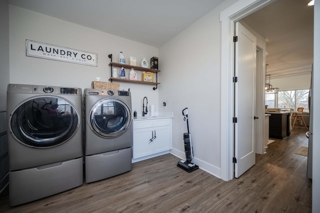 clothes washing area with cabinets, washing machine and dryer, sink, and hardwood / wood-style floors