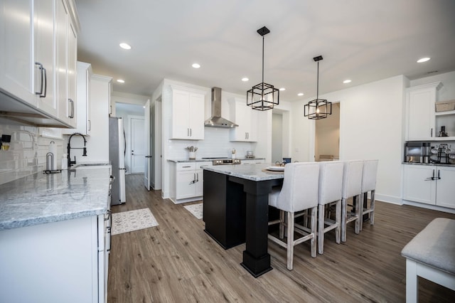 kitchen featuring a kitchen island, white cabinetry, hanging light fixtures, light stone counters, and wall chimney exhaust hood