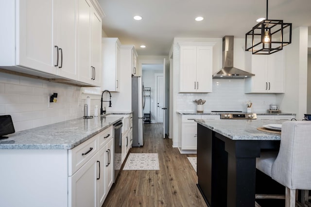 kitchen with hanging light fixtures, white cabinetry, light stone counters, and wall chimney exhaust hood