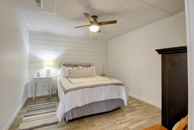 bedroom featuring ceiling fan, a paneled ceiling, wooden walls, and hardwood / wood-style floors