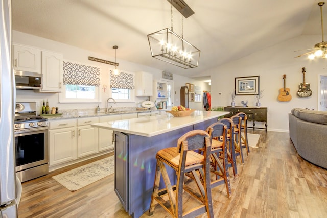 kitchen featuring appliances with stainless steel finishes, white cabinetry, hanging light fixtures, a center island, and a kitchen bar