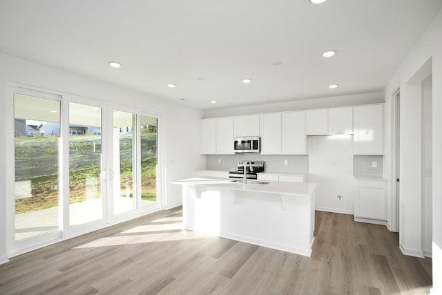 kitchen featuring an island with sink, white cabinetry, sink, stainless steel appliances, and light hardwood / wood-style flooring